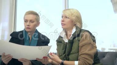 两个女人正在说话，坐在<strong>售楼</strong>处的背景上布置着大楼